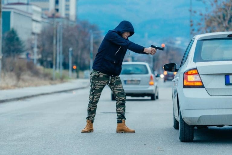 Car hijacker with a gun trying to rob a guy which is sitting in his car. Gorgev / Shutterstock.com
